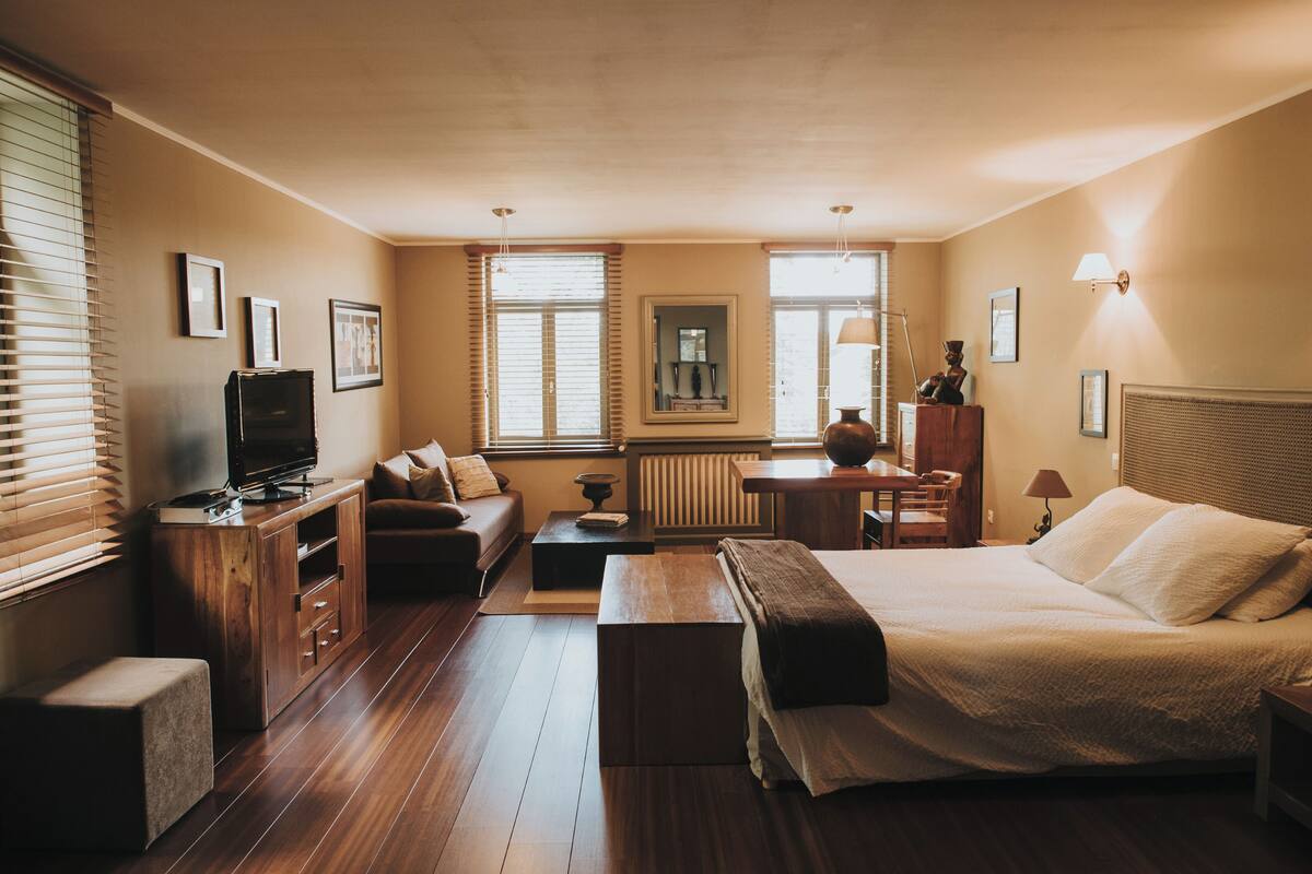 Een hotelkamer met een bed, een bank, een televisie, een tafeltje en een raam met jaloezieën.