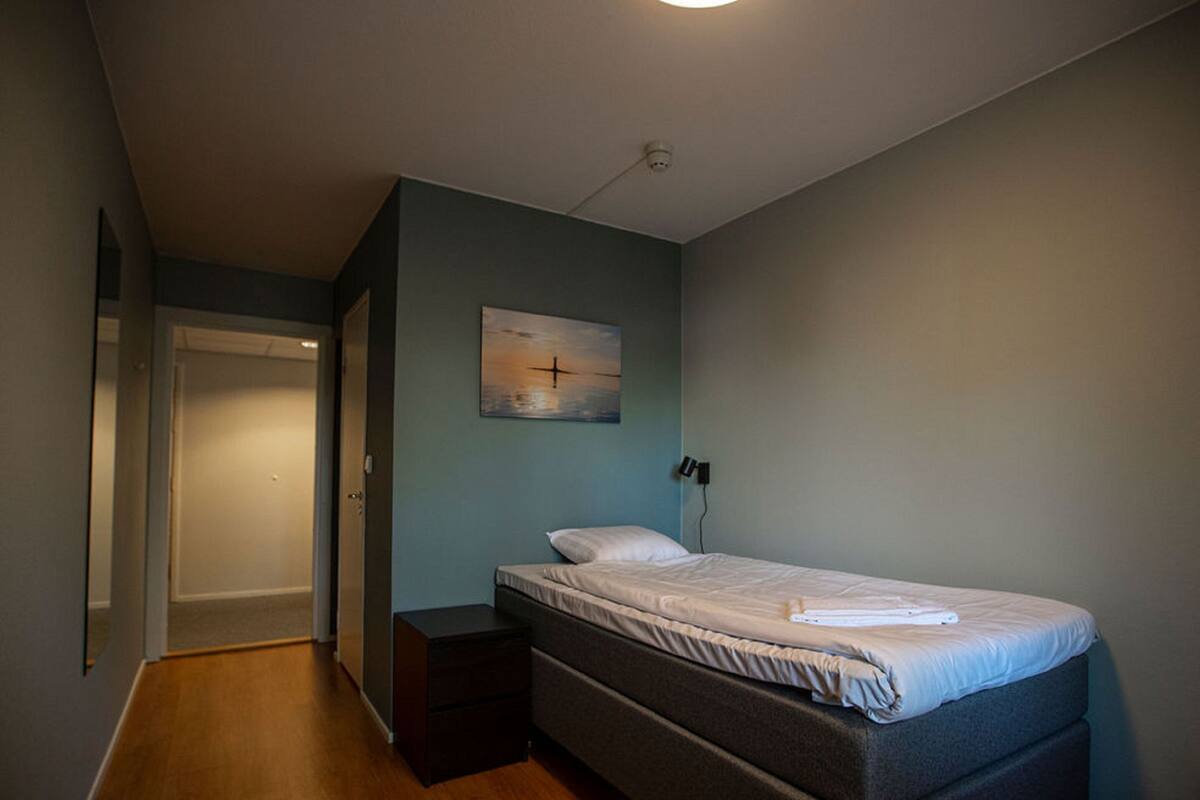 A bedroom with a single bed, a nightstand, a painting on the wall, and a door leading to another room.