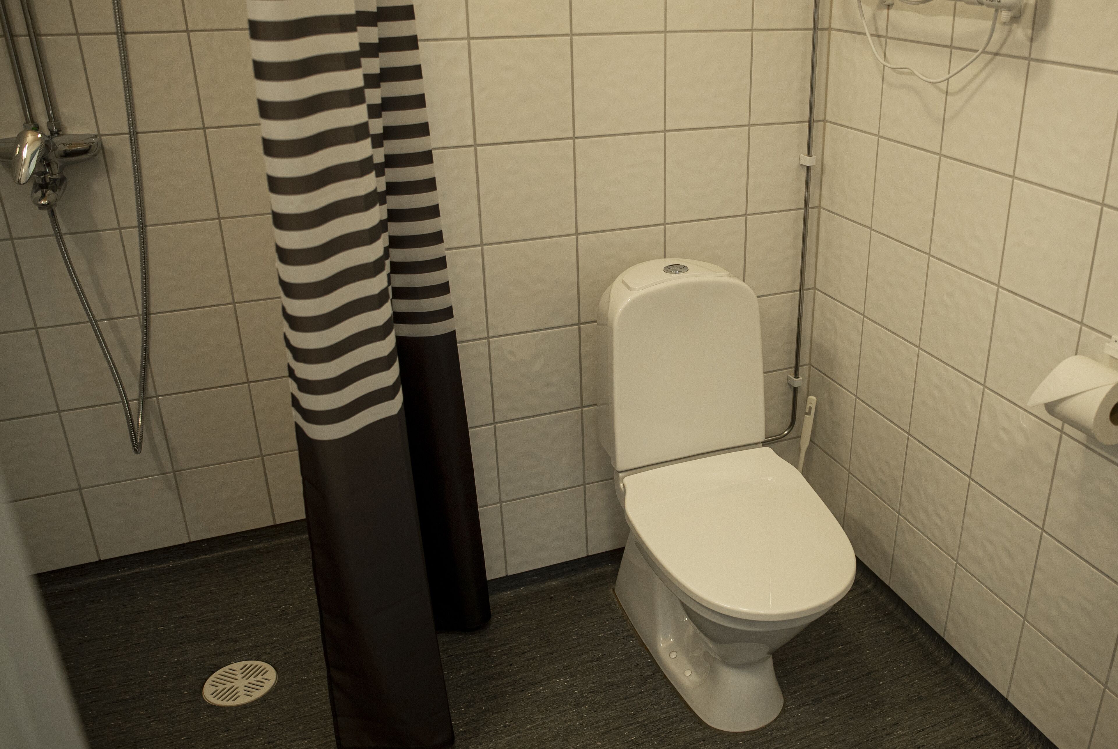 Un bagno piccolo rivestito di piastrelle, con un water bianco, una doccia e un tendaggio a righe.