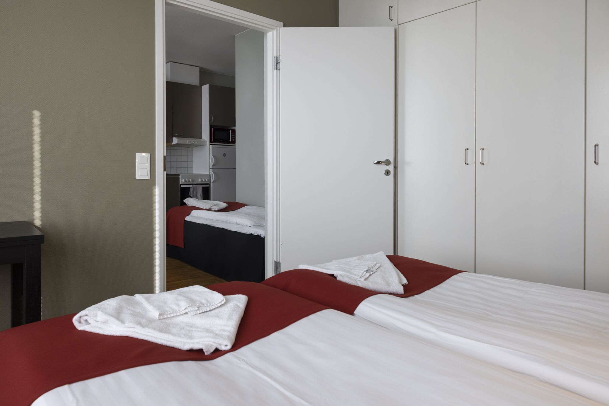 Hotellihuone, jossa on kaksi sänkyä, vaatekaappi ja pieni keittiönurkkaus.