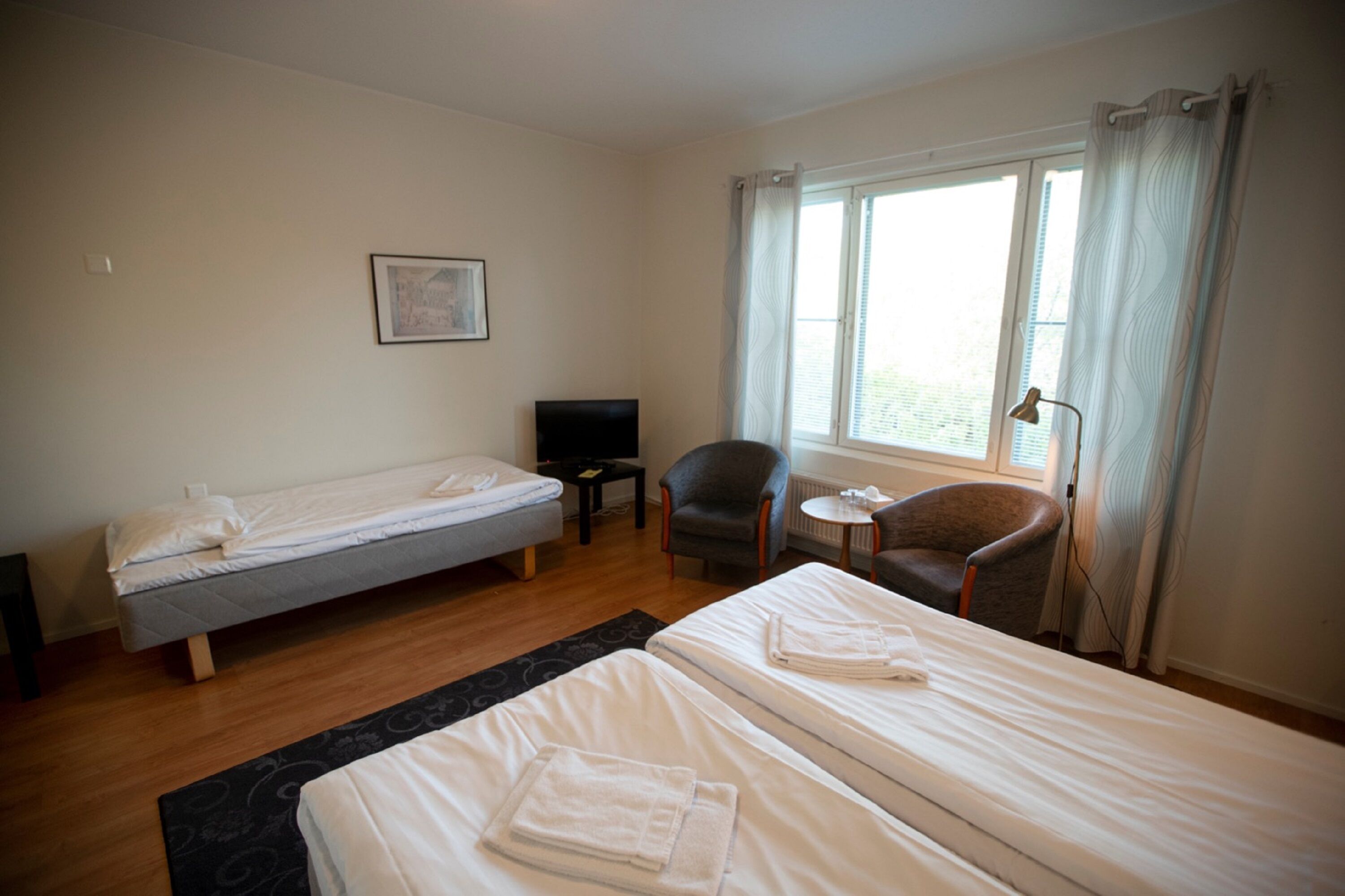 A hotel room with two single beds, a small desk, a chair, and a window with curtains.