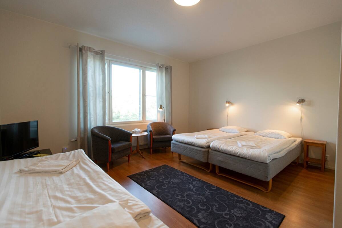 A hotel room with a bed, a desk, a chair, a TV, and a window with curtains.