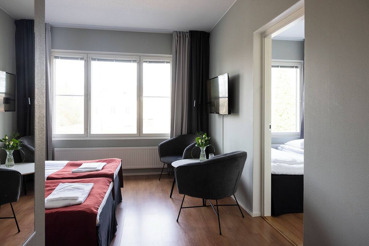 A hotel room with a bed, a desk with a chair, a TV, and a window with curtains.