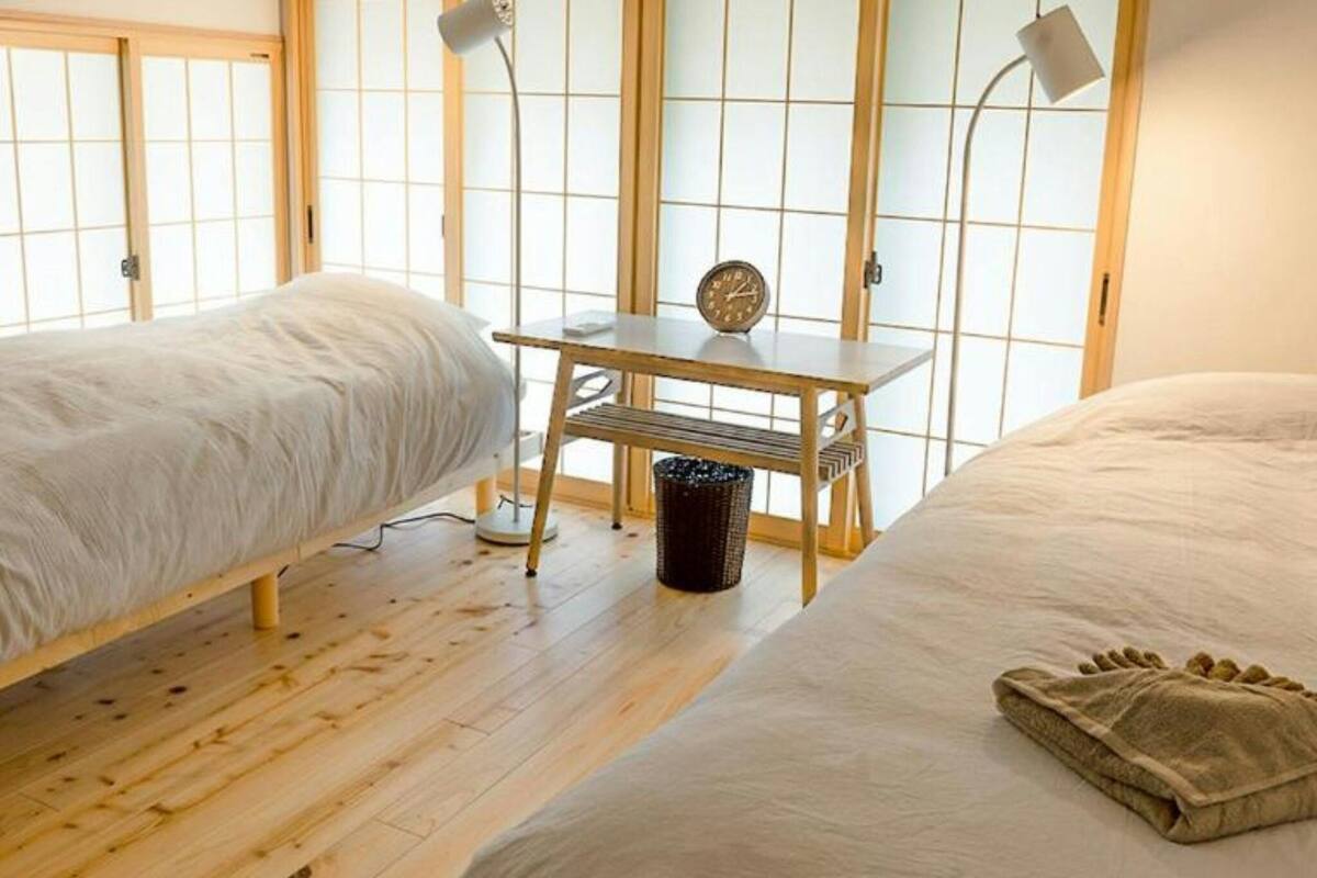 A room with two beds, a small table, a clock, and a trash bin.