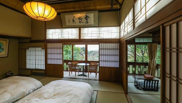 Una habitación tradicional japonesa con suelo de tatami, una mesa baja con sillas y vistas a la vegetación exterior.