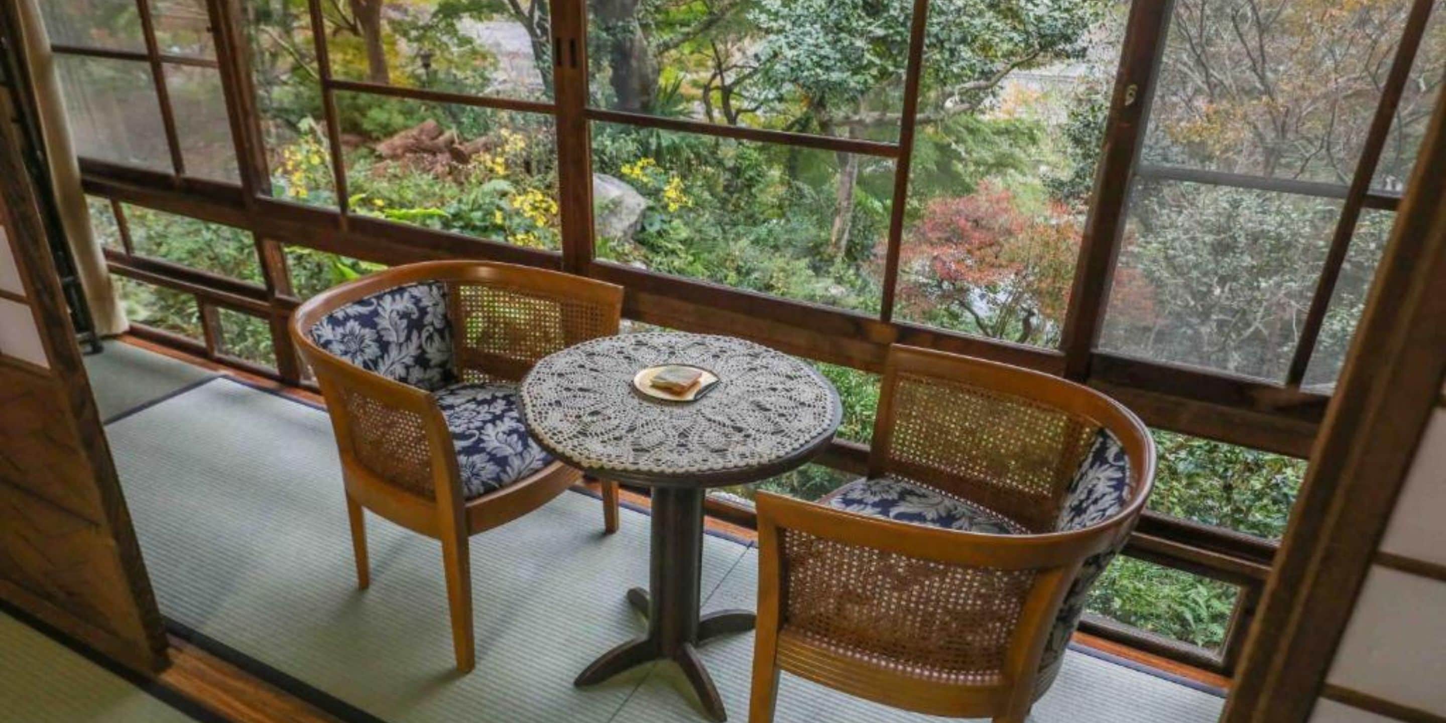Una habitación japonesa tradicional con suelo de tatami, una mesa baja con un tapete tejido y dos sillas con cojines estampados.