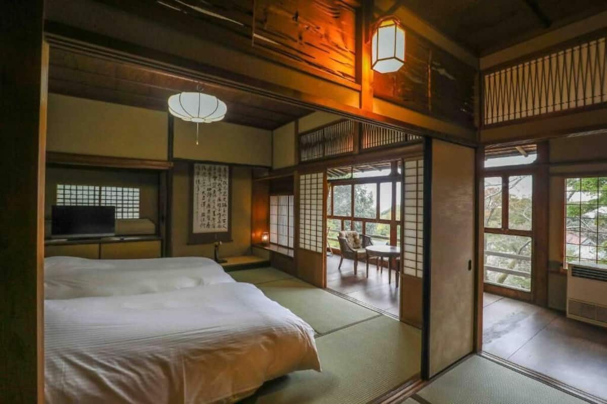 A traditional Japanese room with tatami flooring, a bed, a television, and sliding doors leading to a balcony.