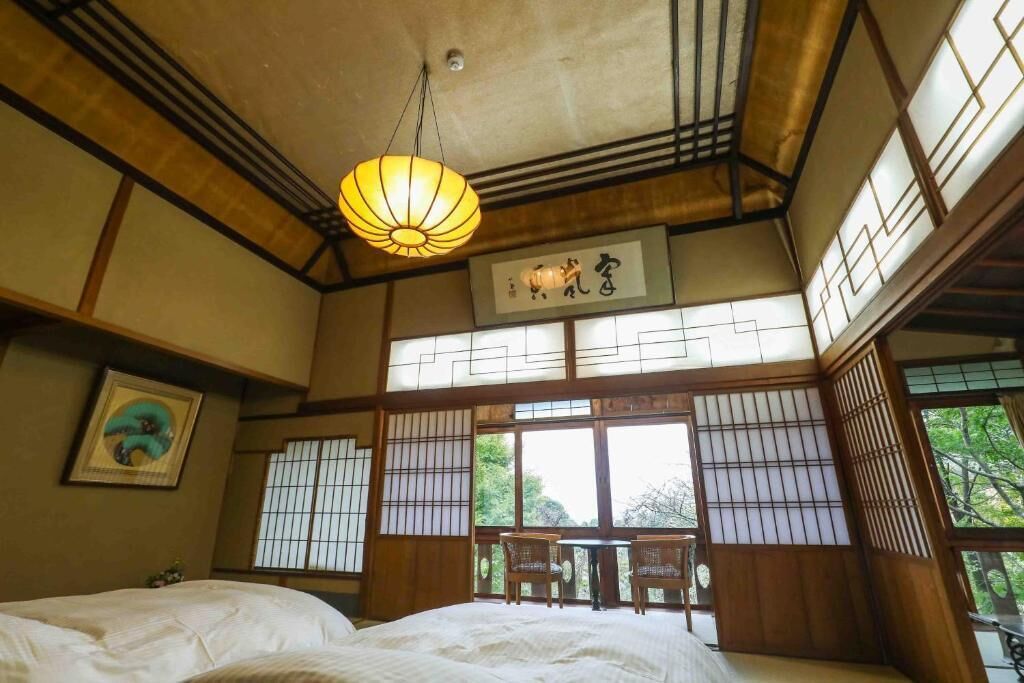 A traditional Japanese-style room with tatami flooring, a bed, a hanging lantern, and a view of the outdoors.