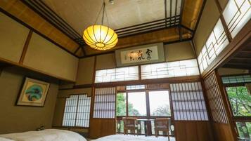 A traditional Japanese-style room with tatami flooring, a bed, a hanging lantern, and a view of the outdoors.