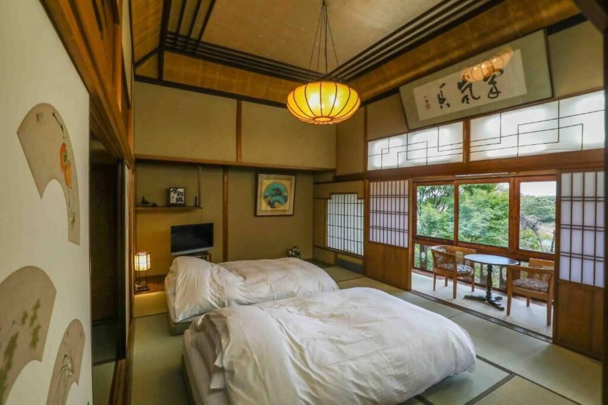 A traditional Japanese-style room with tatami flooring, two beds, a television, and a view of greenery through the sliding doors.