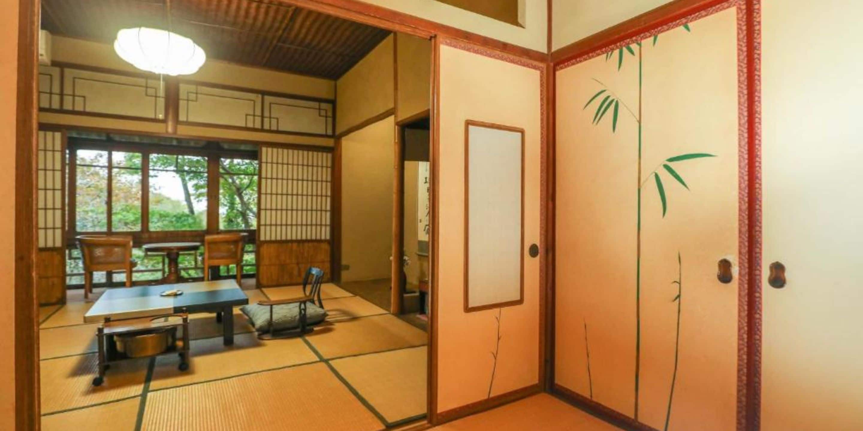 Una habitación tradicional japonesa con suelo de tatami, una mesa baja con cojines y puertas correderas con motivos de bambú.
