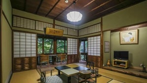 Una habitación japonesa tradicional con suelo de tatami, una mesa baja, sillas y un televisor.
