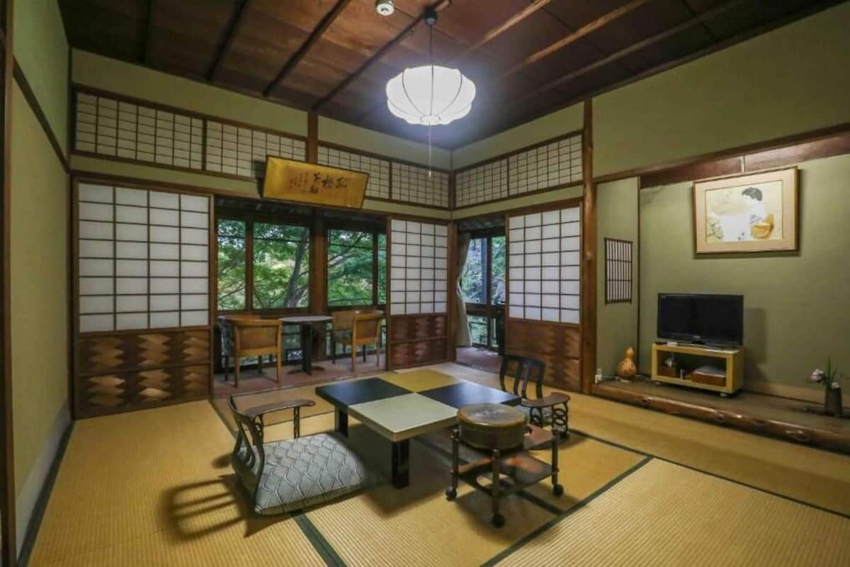 A traditional Japanese room with tatami flooring, a low table, chairs, and a television.