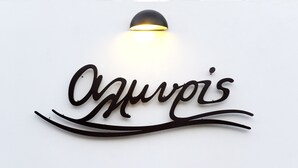A wall-mounted sign with the name "Aquarius" in a cursive script, illuminated by a light fixture above it. - Almyris (Milos)