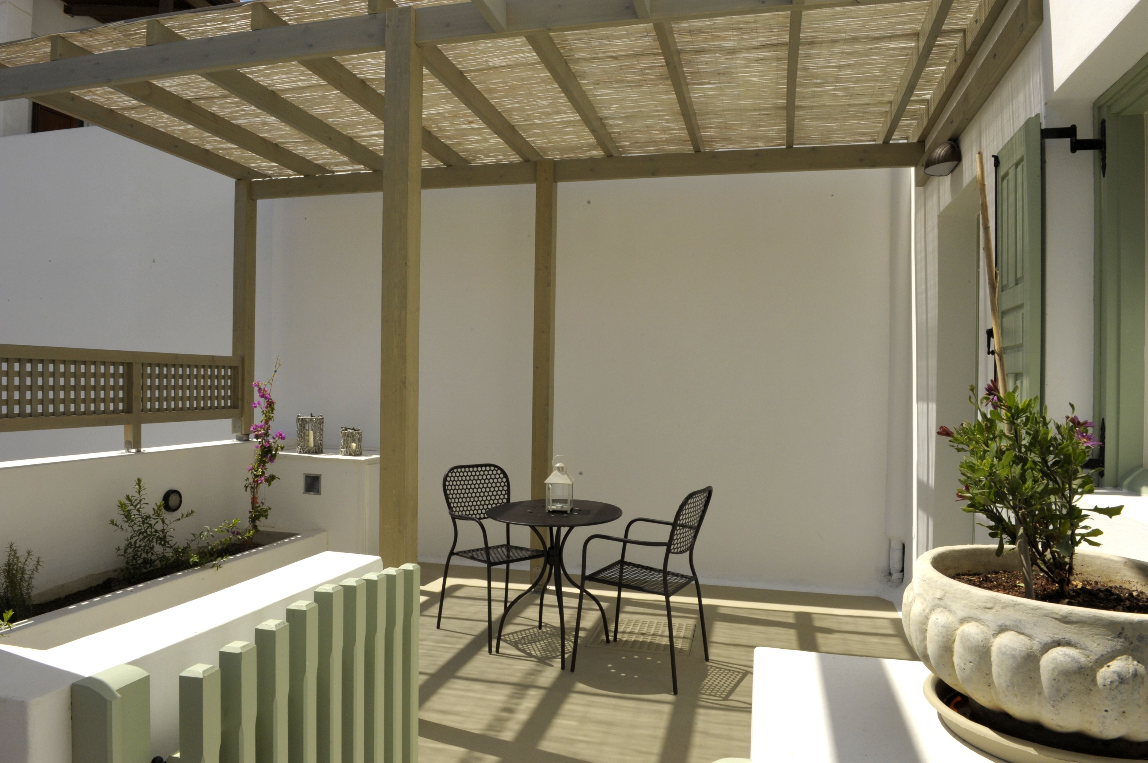 A covered patio area with a table and chairs, a potted plant, and a decorative fence.