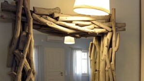 A mirror framed with natural wood branches, a bedside lamp, and a bed in the background. - Almyris (Milos)