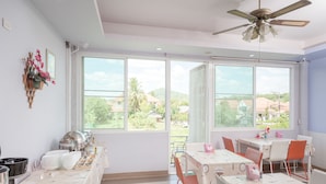Une salle à manger lumineuse, dotée de grandes fenêtres, d’un ventilateur de plafond et d’un buffet.
