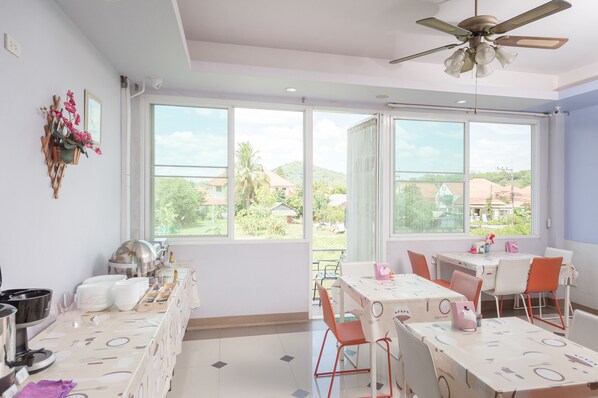 Un comedor luminoso con ventanas amplias, ventilador de techo y mesas de buffet.