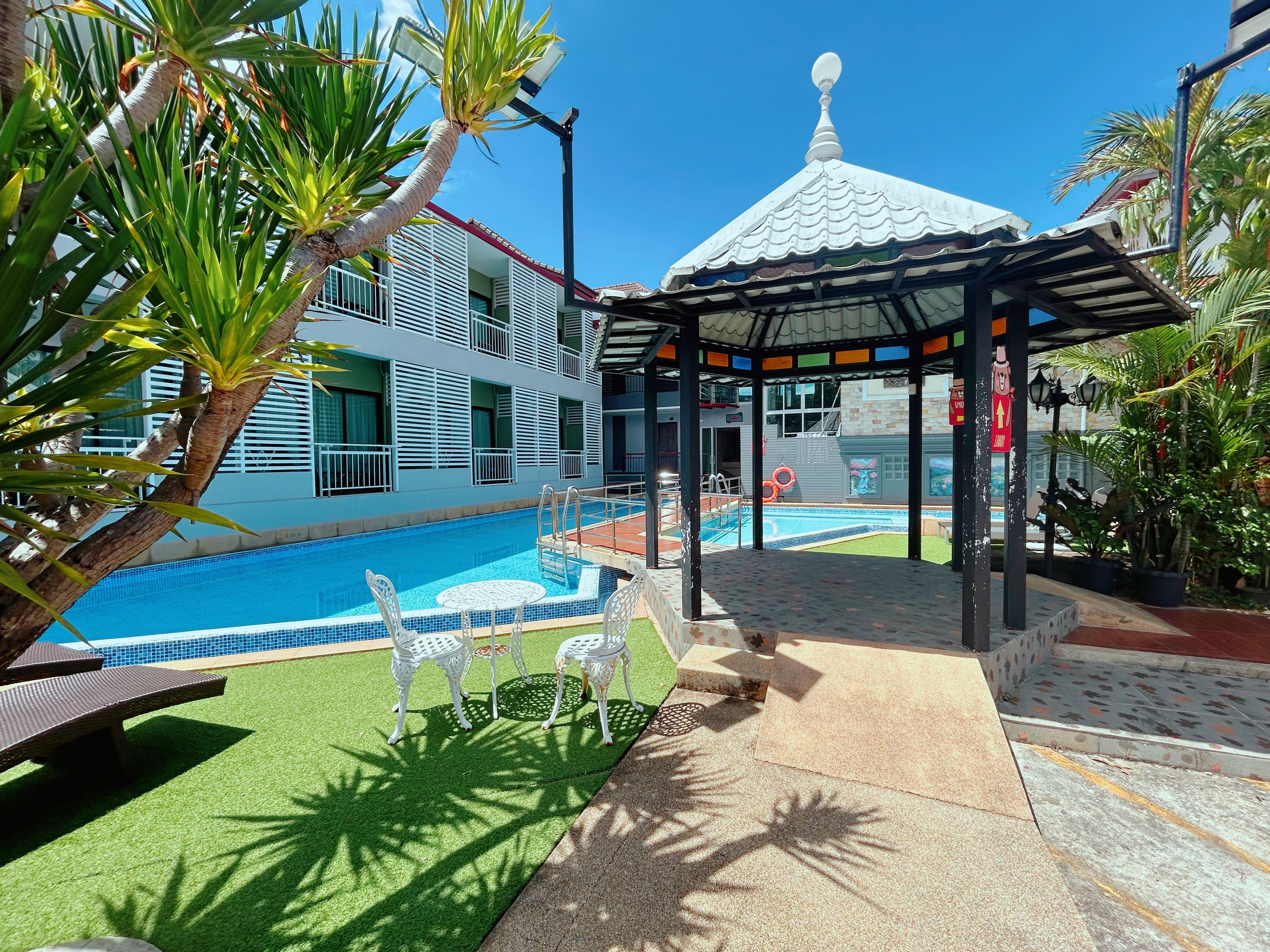 A pool area with a gazebo, lounge chairs, and a building with balconies.