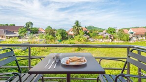 Une table dressée avec des aliments pour le petit-déjeuner et une tasse, donnant sur un paysage verdoyant parsemé de maisons.