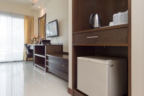 A hotel room with a wooden desk, a flat-screen TV, a refrigerator, and a coffee maker. - Chayadol Resort (Chiang Rai)