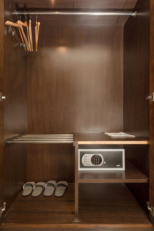 A walk-in closet with wooden hangers, a shoe rack, and a built-in safe. - Chayadol Resort (Chiang Rai)