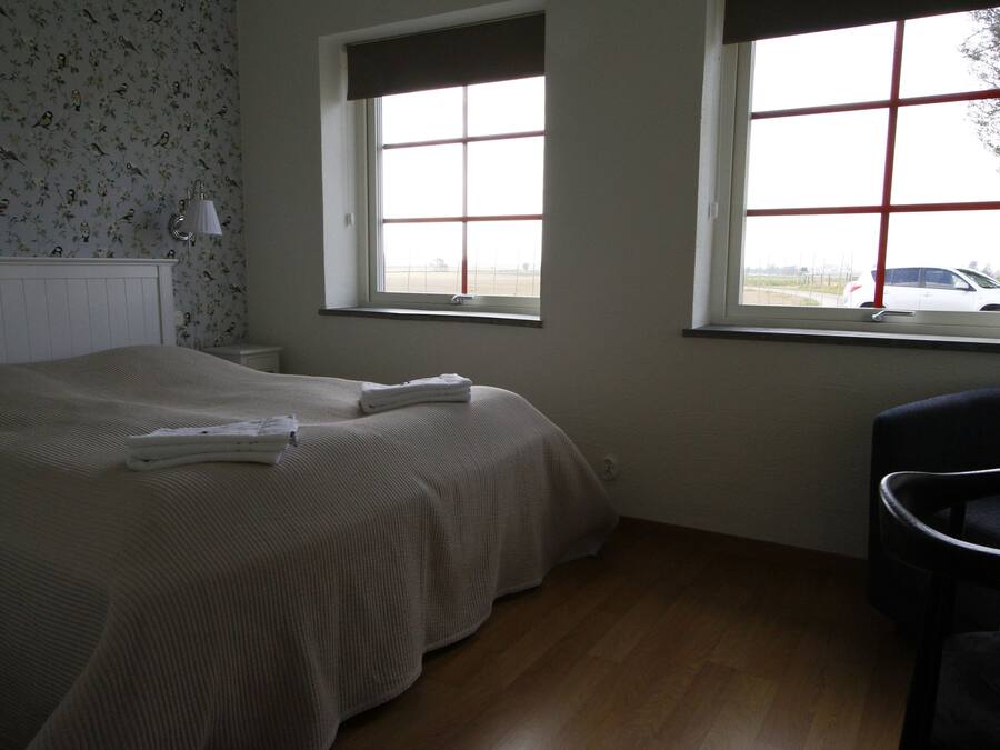 Une chambre avec deux lits, une fenêtre donnant sur une voiture et une chaise.