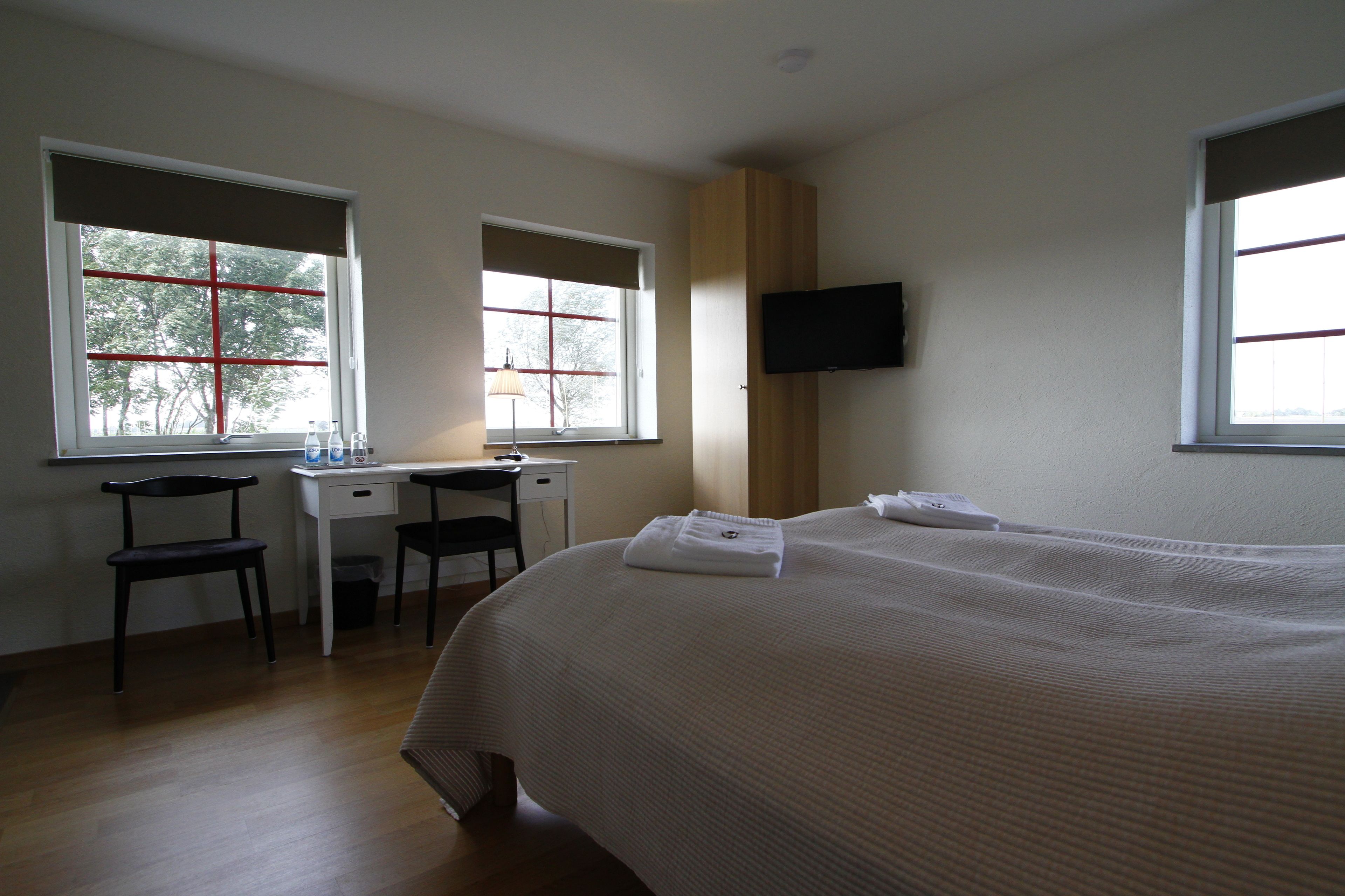 A hotel room with a large bed, a desk, two chairs, a TV, and windows with blinds.