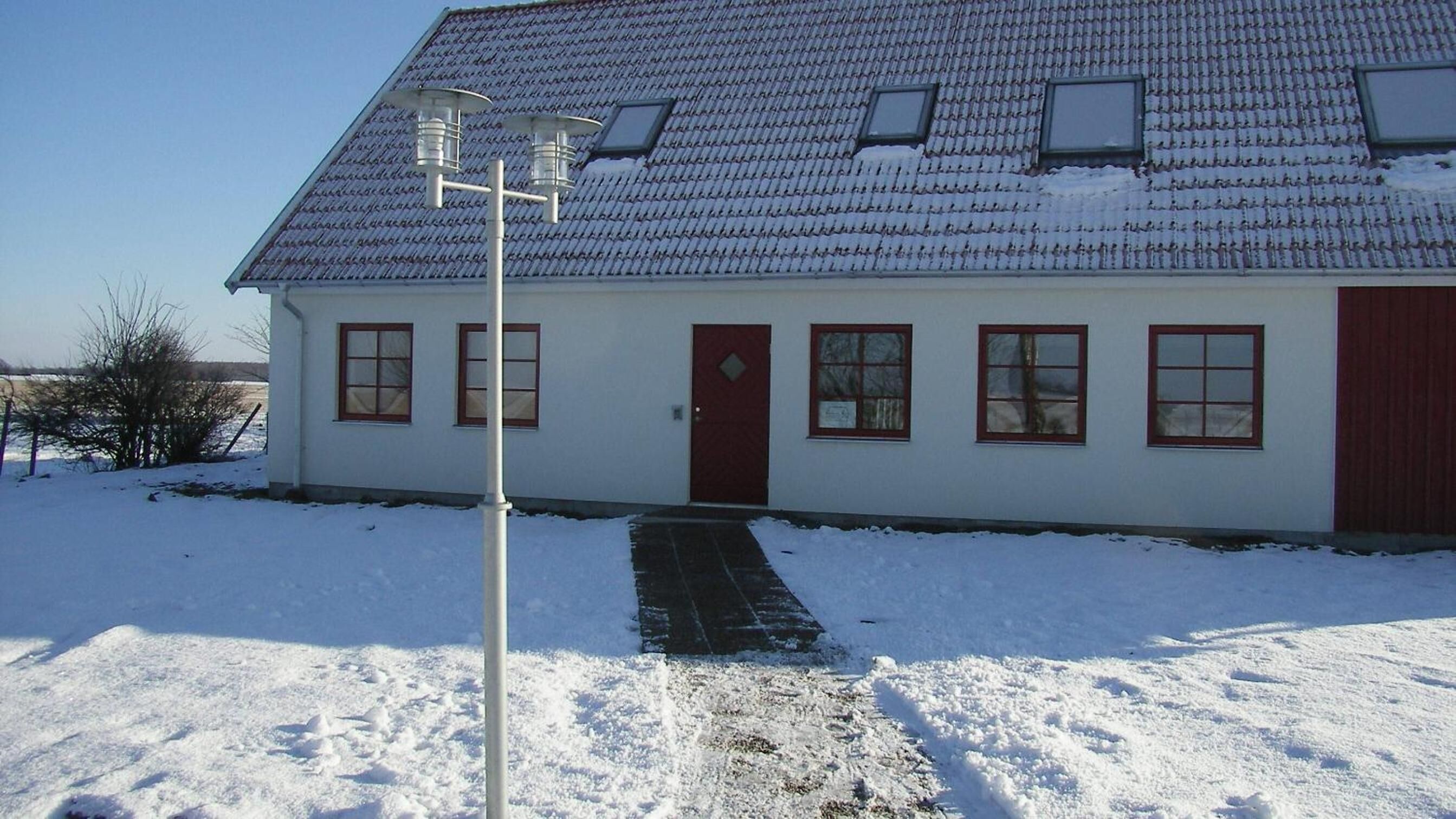 Un bâtiment blanc avec une porte rouge, de nombreuses fenêtres et un toit recouvert de neige.