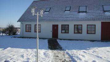 A white building with a red door, multiple windows, and a snow-covered roof.