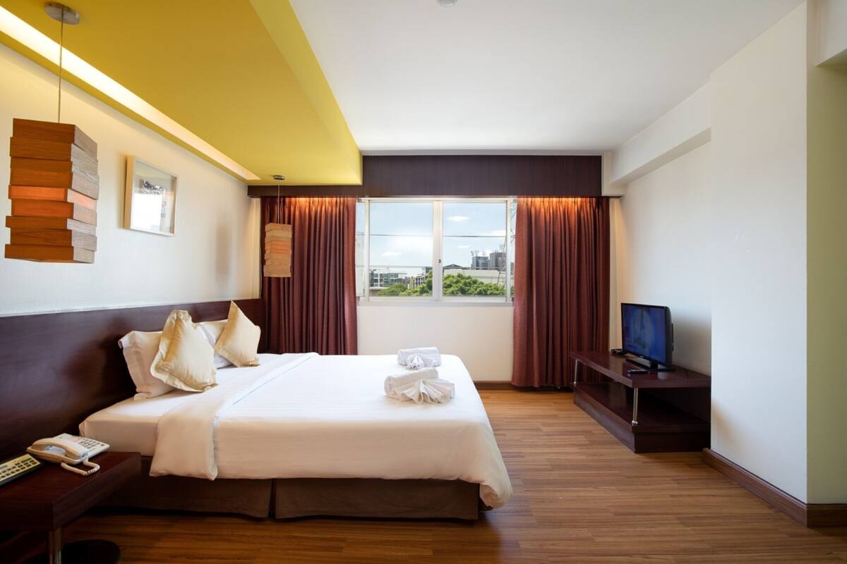 A hotel room with a bed, a TV, a desk with a phone, and a window with curtains.