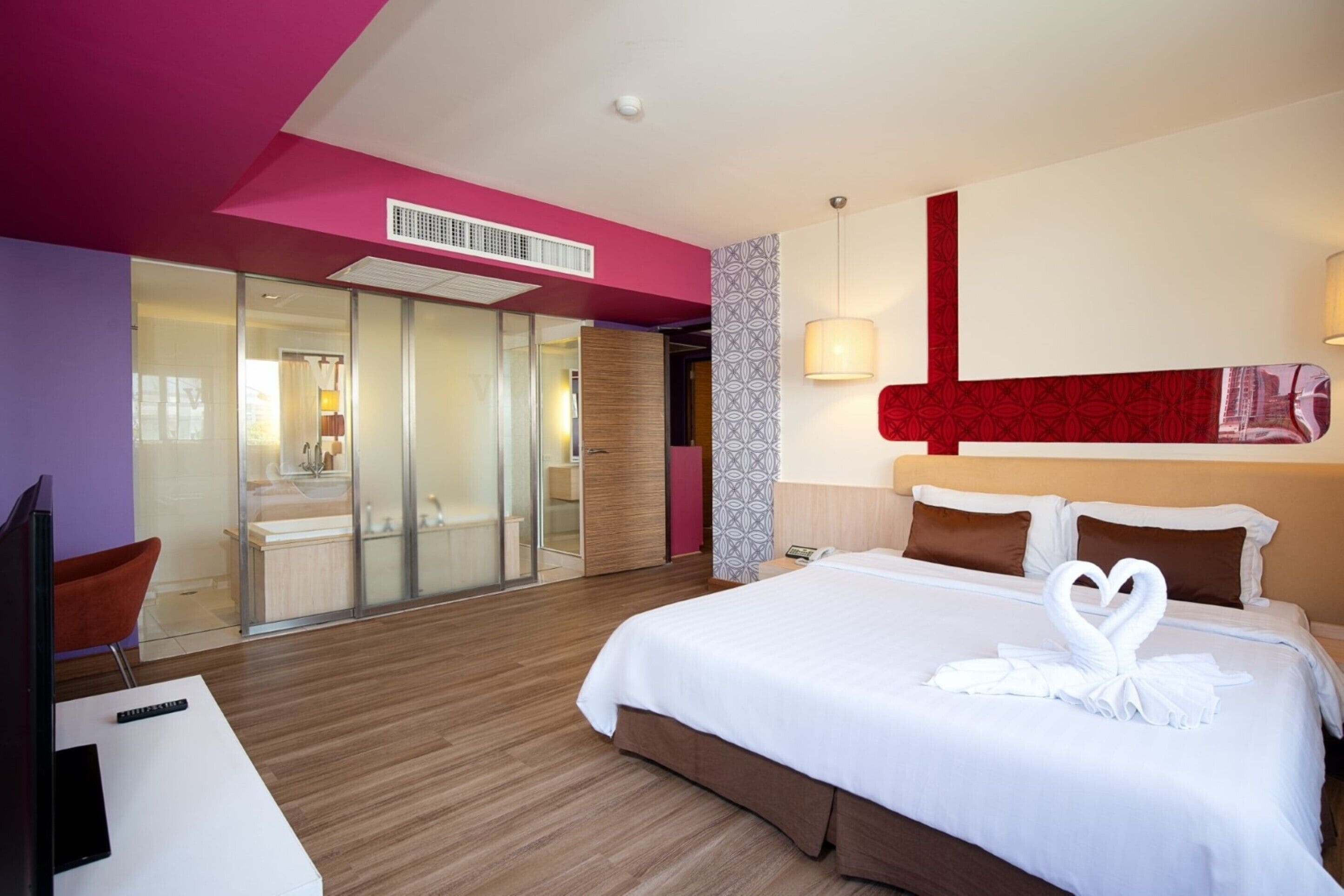 A modern hotel room with a large bed, a desk, and a glass-enclosed bathroom.