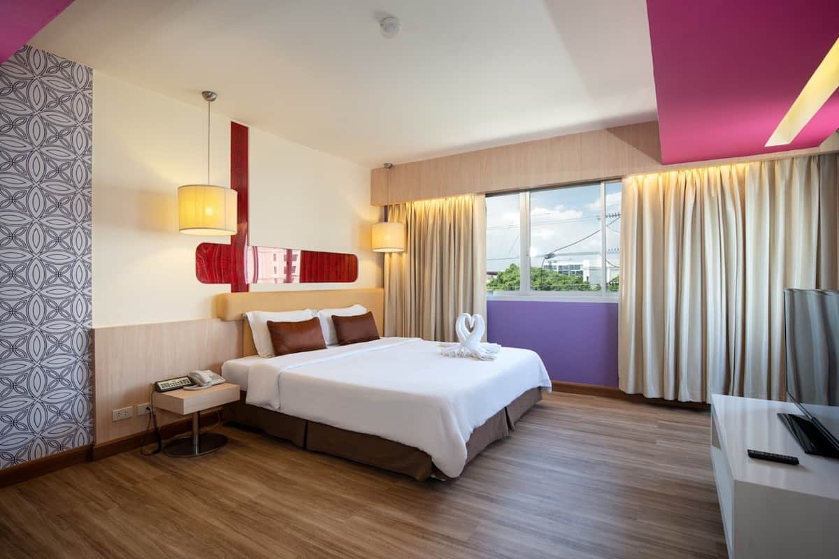 A modern hotel room with a large bed, bedside tables, a desk, and a TV.