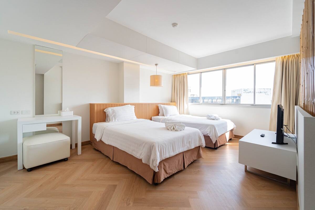 A modern hotel room with two beds, a desk, a chair, and a TV.
