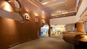 A modern hotel lobby with a curved wall design, a second-floor balcony, and a seating area with round tables. - Veronica Residence (Bangkok)