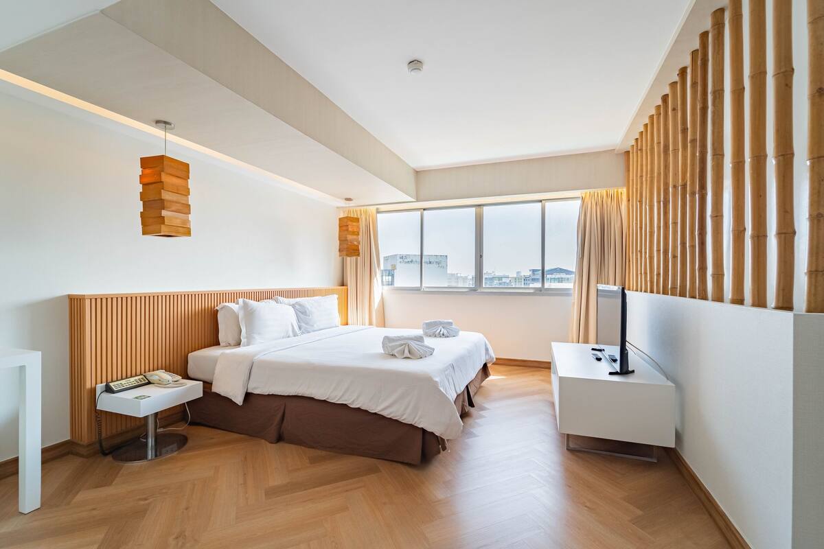 A modern hotel room with a large bed, bedside tables, a flat-screen TV, and a city view.