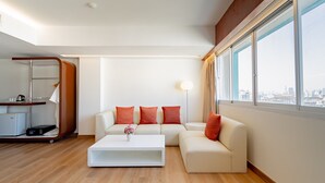 A modern living room with a sectional sofa, a coffee table, and a large window offering a city view. - Veronica Residence (Bangkok)