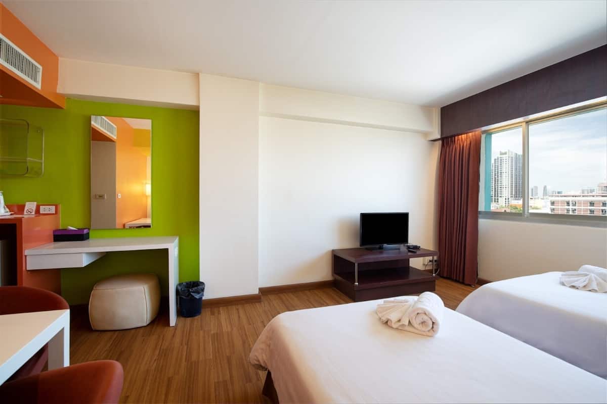 A hotel room with a bed, a desk, a television, and a window with a city view.