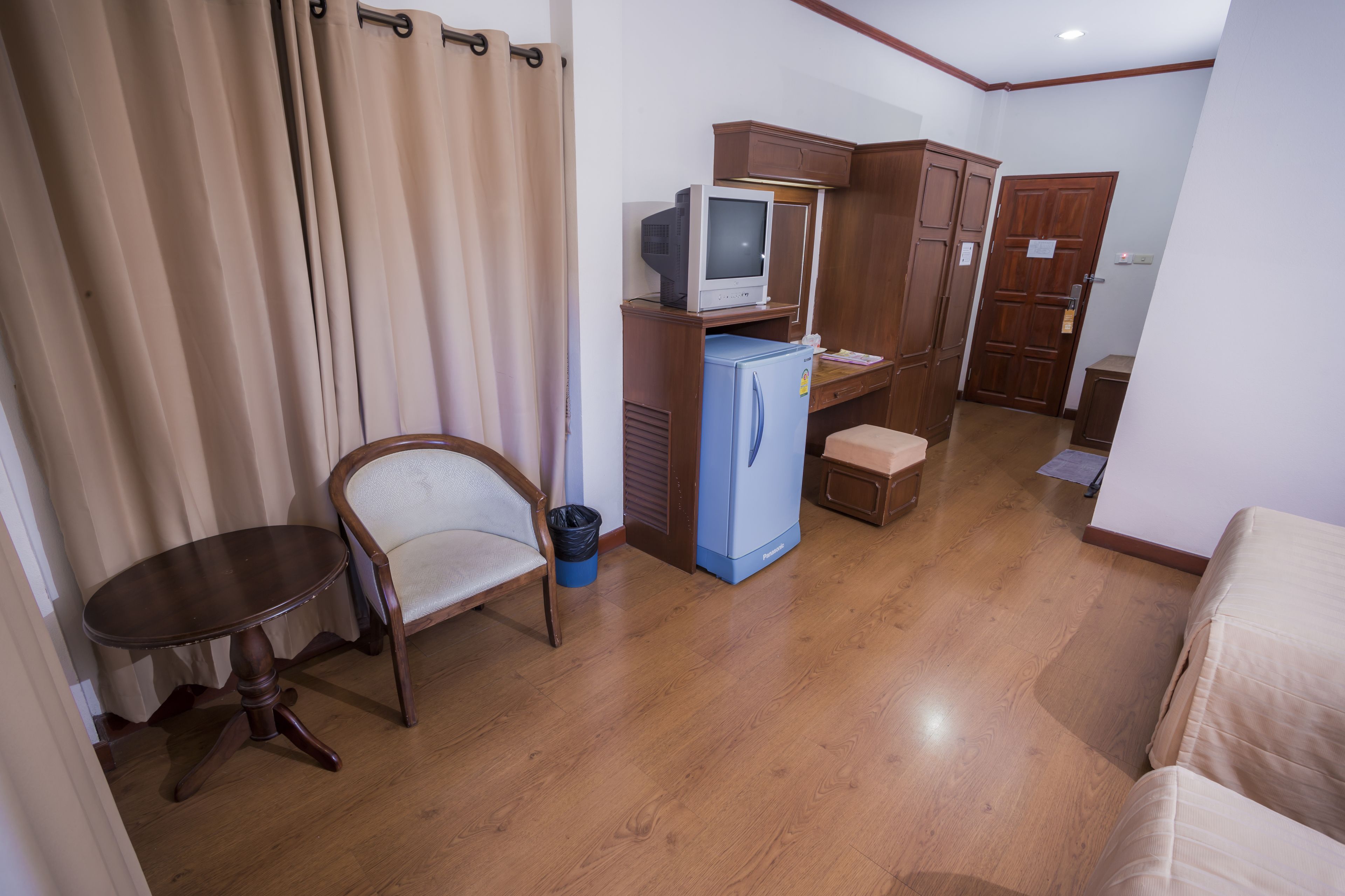 A compact living space with a television, a refrigerator, a wooden cabinet, a chair, and a small table.