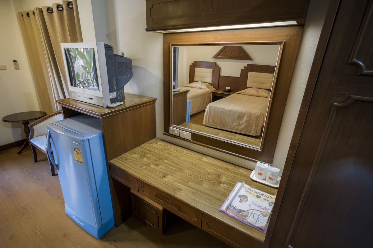 A hotel room with a wooden desk, a television, a mirror, and a bed.