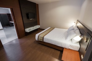 Habitació d'hotel moderna amb sòl de fusta, llit amb roba de llit blanca, una taula de nit, televisió penjada a la paret i una petita estantèlia.