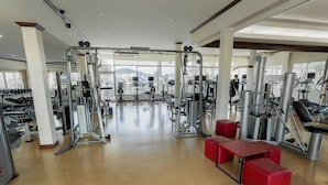 Et fitnesscenter med forskellige træningsmaskiner, bænke og et stort vindue med udsigt udendørs.