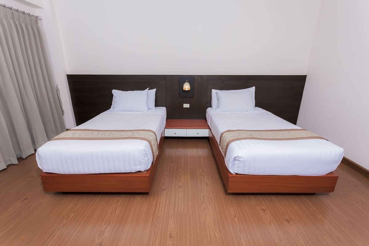 A double room with two beds, a wooden headboard, a small table, and a wall-mounted light.