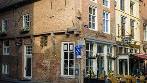 Un bâtiment historique à la façade en briques, doté de nombreuses fenêtres et d’un espace extérieur aménagé avec des chaises.