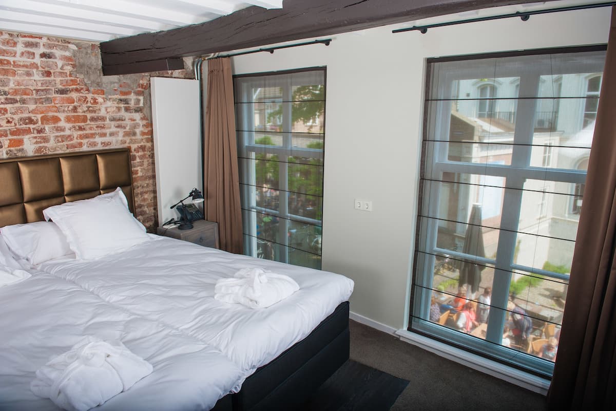 Een hotelkamer met een groot bed, een bakstenen muur en grote ramen met gordijnen.