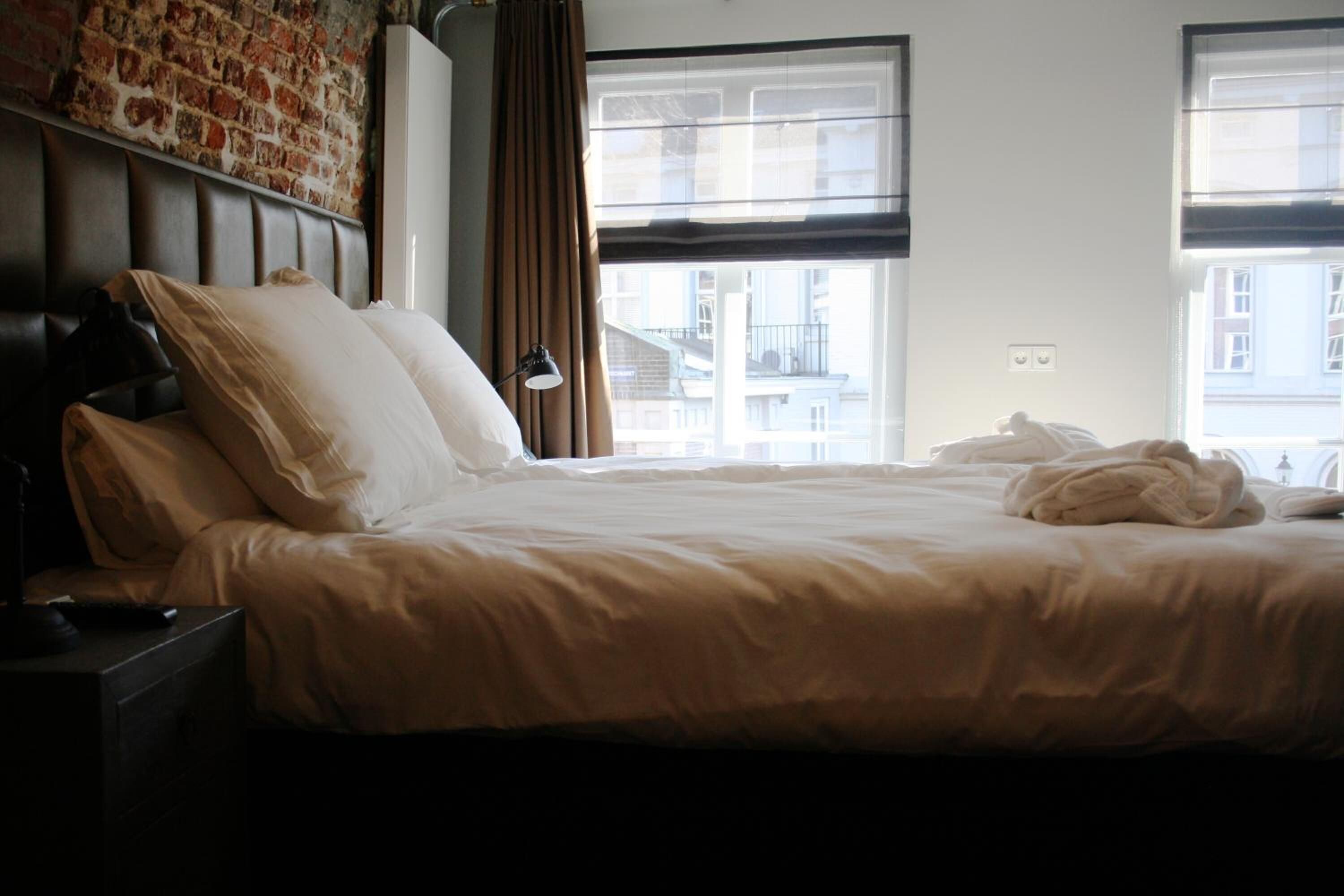 Une chambre d’hôtel avec un grand lit, une tête de lit, une table de chevet, une lampe et une vue sur les bâtiments par la fenêtre.