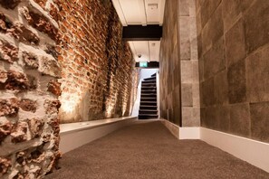 Ein Korridor mit einer Backsteinwand auf der einen Seite und einer Steinwand auf der anderen, der zu einer Treppe führt.