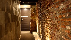 Un couloir étroit, avec un mur de briques d’un côté et un mur recouvert de carreaux de l’autre, qui mène à une porte.