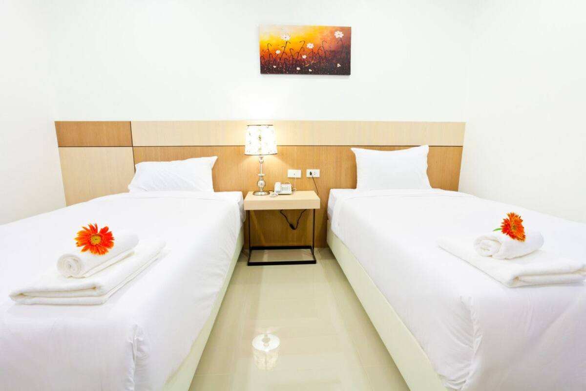 A hotel room with two beds, a nightstand, a lamp, and a painting on the wall.