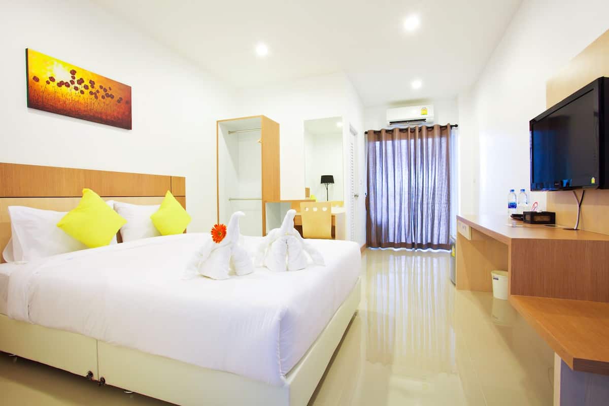 A hotel room with a large bed, a TV, a desk, and a bathroom visible through a glass door.